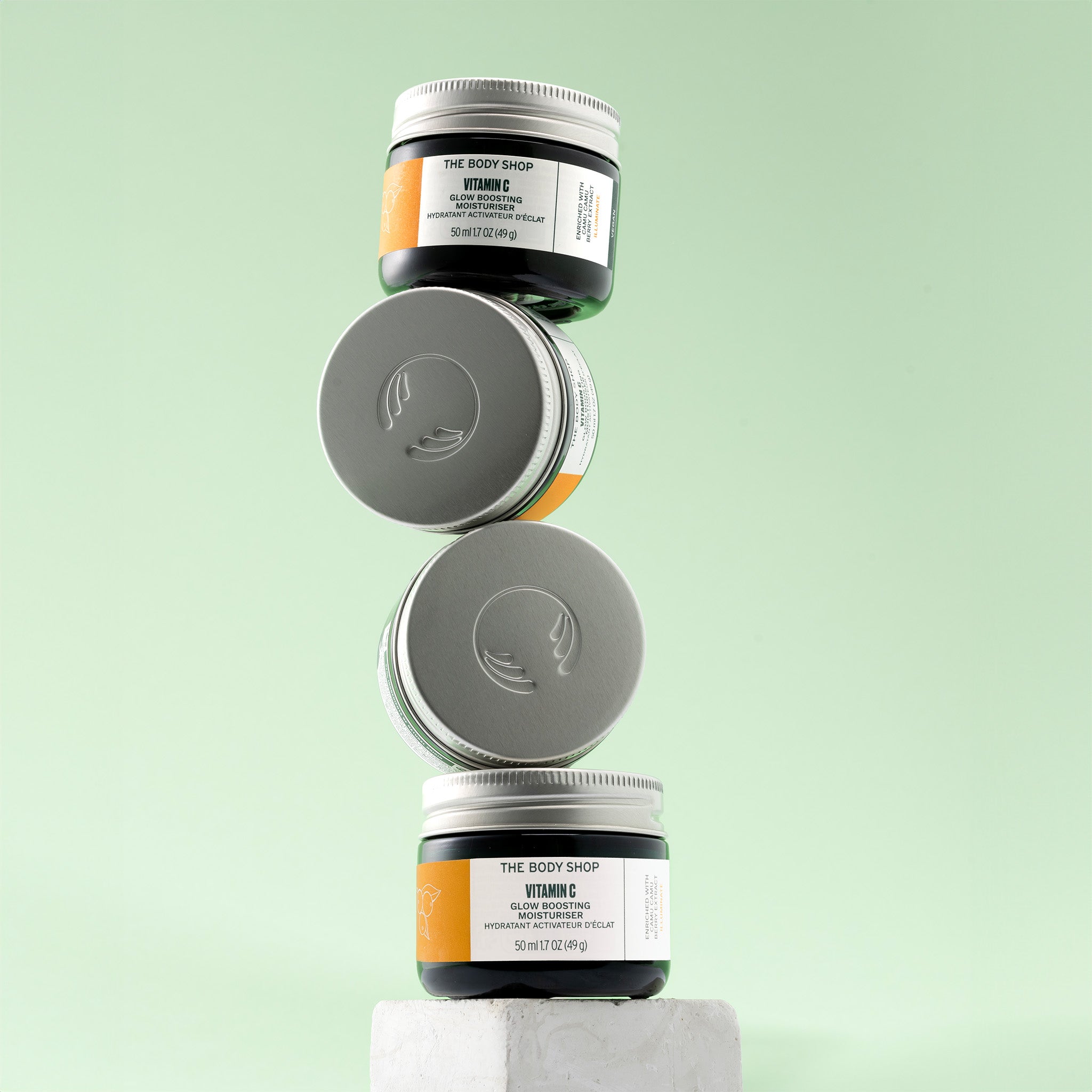 Stack of The Body Shop Glow Boosting Moisturiser jars on a light green background