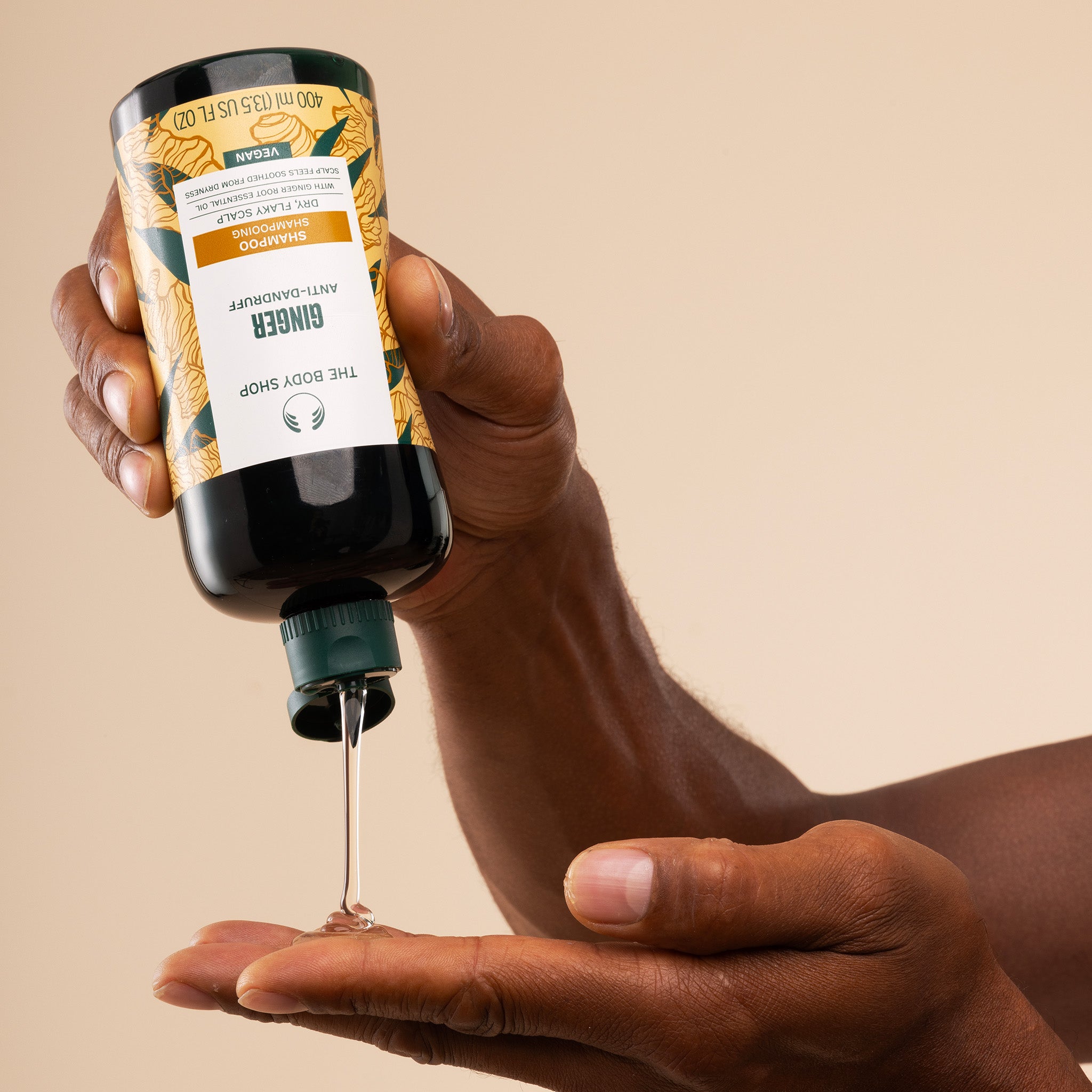 Hand holding a bottle of Ginger Shampoo with a beige background - The Body Shop Ginger Anti-dandruff Shampoo
